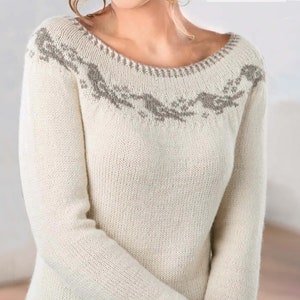 Pode incluir: Um suéter de malha branco com um padrão geométrico cinza ao redor da gola.