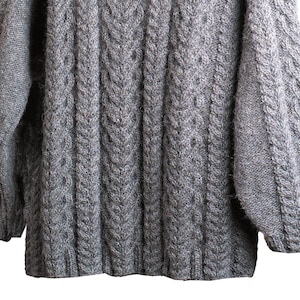 May include: A gray cable knit sweater with a ribbed texture. The sweater has long sleeves and a crew neck.