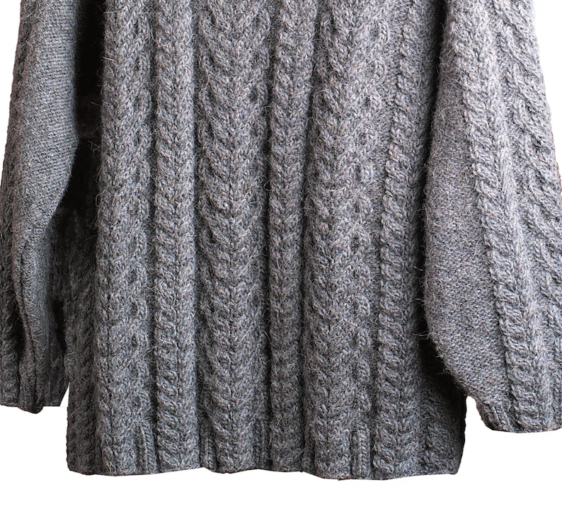 May include: A gray cable knit sweater with a ribbed texture. The sweater has long sleeves and a crew neck.