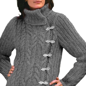 Puede incluir: Un suéter gris de punto trenzado con cuello alto y plegado y cierres de palanca plateados. El suéter presenta un diseño de punto trenzado texturizado en la parte delantera y las mangas. Las mangas largas y el cuello alto brindan calidez y estilo.