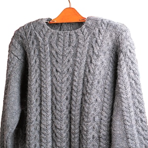 May include: A gray cable knit sweater hanging on a wooden hanger. The sweater has a classic crew neck and a textured pattern.