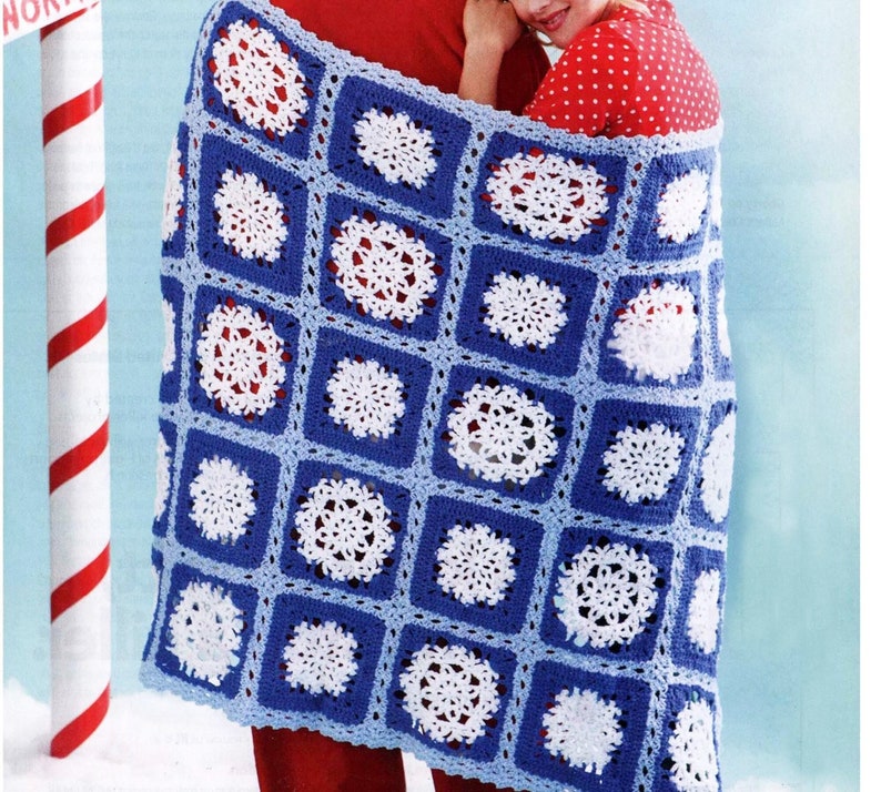 May include: A blue and white crocheted blanket with a snowflake pattern. The blanket is folded and draped over two people.