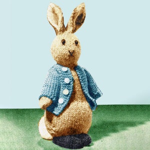 May include: A knitted brown bunny rabbit wearing a blue knitted cardigan with white buttons. The bunny is standing on a green surface.