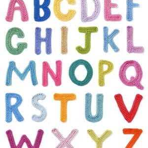 Może przedstawiać: Kolorowy alfabet wykonany z dzianiny szydełkowej. Każda litera ma inny kolor, w tym różowy, niebieski, zielony, żółty, pomarańczowy i fioletowy.