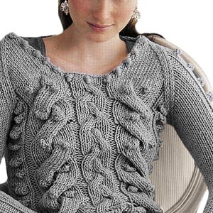 May include: A gray knitted sweater with a textured cable knit design and bobble details. The long-sleeved sweater has a scoop neckline and is made of a soft, warm material. The sweater is a stylish and comfortable garment.
