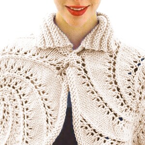 May include: Cream-coloured knitted bolero with a decorative openwork pattern. The bolero features a shawl collar and is fastened with a metal clasp. The knitwear has a textured appearance and is suitable for layering.