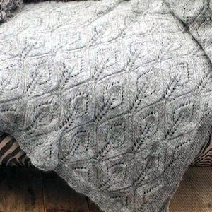 Puede incluir: Una manta de punto gris con un delicado patrón de hojas. La manta está drapeada sobre una silla con estampado de cebra.