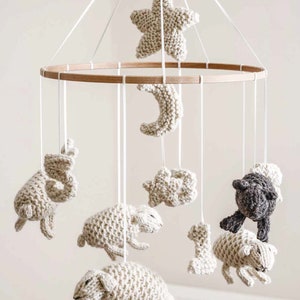 May include: A wooden baby mobile with a white knitted star, moon, and sheep. There are also two small stars and a black sheep.