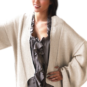 Puede incluir: Un cárdigan crema con frente abierto y diseño de punto texturizado. El cárdigan tiene mangas anchas y un ajuste relajado. La modelo lleva una blusa gris debajo. El cárdigan es una prenda versátil para combinar.