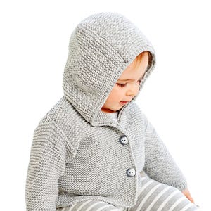 May include: A light gray knitted hooded cardigan with two buttons. The baby is wearing the cardigan over a light gray and white striped outfit. The cardigan is made of a soft, textured knit fabric.