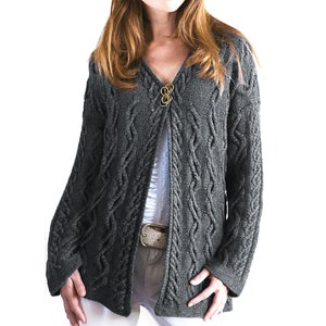 Könnte beinhalten: Ein grauer Strickpullover mit Zopfmuster, V-Ausschnitt und goldfarbenem Knopfverschluss.