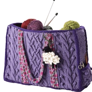 Puede incluir: Un bolso tote tejido de color púrpura con diseño de punto trenzado, que contiene ovillos de lana y agujas de tejer. El bolso tiene un pequeño bolsillo con tijeras y un adorno de oveja. Ideal para llevar suministros de tejido.