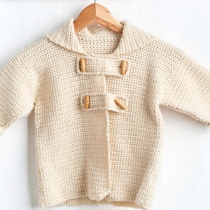 May include: A cream-colored crocheted cardigan with wooden toggle buttons. The cardigan has a collar and long sleeves.