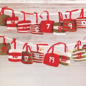 May include: A handmade Christmas advent calendar with 24 small, knitted bags in red, white, and green. Each bag is numbered and suspended from a white string with red ribbon handles, creating a festive holiday decoration.