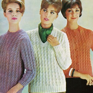 May include: Three women wearing different cable knit sweaters. The sweaters are in shades of purple, white, and orange. The women are all smiling and looking at the camera.