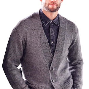 May include: A grey knitted cardigan with a shawl collar and two front pockets. The sweater has a button-up closure and is worn over a dark denim shirt. The knitwear appears to be a medium weight.