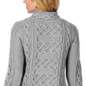 Puede incluir: Un suéter gris tejido con trenzas y cuello alto. La parte trasera del suéter presenta un diseño detallado de nudo celta. Las mangas y los laterales tienen un patrón de trenzas texturizado. El suéter está hecho de un material suave y tejido.