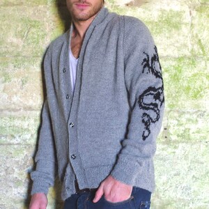 May include: A gray knitted cardigan with a black dragon design on the sleeve. The cardigan has a shawl collar and a button closure.