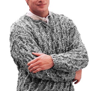 Könnte beinhalten: Ein grau-weiß strukturierter Strickpullover mit Rundhalsausschnitt. Der Pullover hat ein dickes Zopfmuster und lange Ärmel. Die Person trägt darunter ein weißes Hemd mit Kragen.