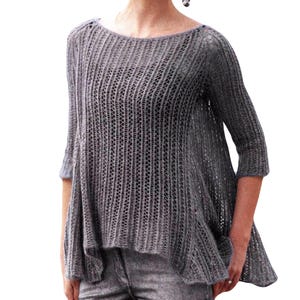 May include: A grey knitted jumper with a loose fit and a slightly longer back hem. The jumper has a delicate openwork pattern and a round neckline.