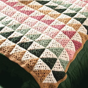 May include: A crocheted blanket with a geometric pattern of triangles in shades of pink, green, brown, and white. The blanket is made with a variety of stitches and textures, creating a unique and interesting design.