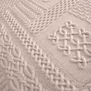 Peut inclure: Une couverture en tricot beige avec différents motifs en tricot torsadé. La couverture est faite de fil doux et confortable et est parfaite pour ajouter de la chaleur et de la texture à n'importe quelle pièce.