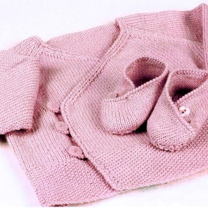 May include: A pink knitted baby cardigan with button fastenings and matching knitted booties.