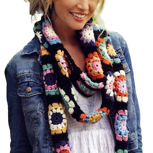 Può includere: Una sciarpa all'uncinetto composta da una serie di granny square floreali multicolori uniti da filato nero. La sciarpa presenta una vivace tavolozza di motivi circolari rosa, arancioni, gialli, blu e bianchi in un design ad anello.