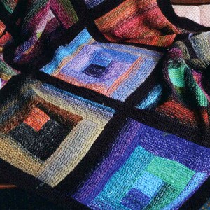 May include: A colorful knitted throw blanket with a geometric pattern of squares within squares. The blanket is made with a variety of shades of blue, green, purple, and orange yarn.