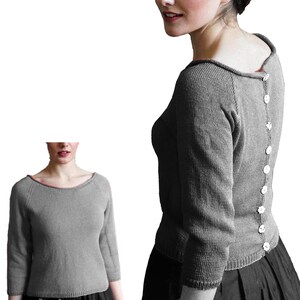 May include: A gray sweater with a boat neck and three-quarter sleeves. The back of the sweater features a row of white buttons. The sweater is shown on a person, with a second image of the sweater on a mannequin.