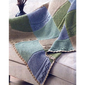 Peut inclure: Une couverture en patchwork tricotée dans des tons de vert, bleu et beige. La couverture est faite de différents points texturés et est drapée sur un canapé.