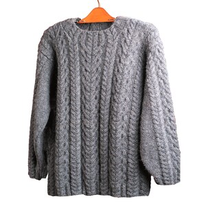 May include: A gray cable knit sweater with a crew neck. The sweater is hanging on a wooden hanger.