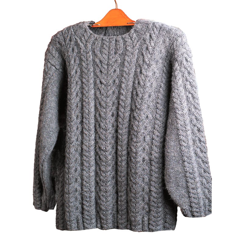 May include: A gray cable knit sweater with a crew neck. The sweater is hanging on a wooden hanger.