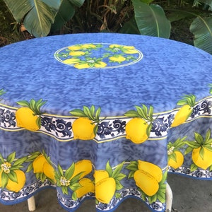 May include: A round blue tablecloth with a lemon design. The tablecloth features a repeating pattern of yellow lemons with green leaves and white flowers. The border has a decorative blue and white design.