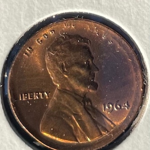 Può includere: Una moneta da un centesimo americana in rame del 1964 con le parole "IN GOD WE TRUST" e "LIBERTY" sul dritto. La moneta presenta un profilo di Abraham Lincoln.