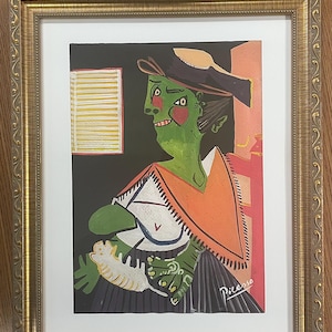 以下が含まれることがあります： ピカソの絵画の額入りプリント。白いショールとオレンジ色のラップを身にまとい、白い生き物を抱えた緑色の肌の人物が描かれています。黒い背景に黄色い窓が配置され、金色のフレームに収められています。