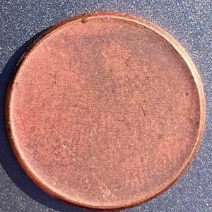 Puede incluir: Una moneda de un centavo de color cobre con una superficie lisa. La moneda tiene un aspecto ligeramente desgastado.