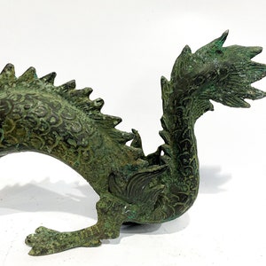 May include: A detailed bronze dragon sculpture with a verdigris finish. The dragon features intricate scale and fin details, with a curved body and a raised claw. The sculpture is a decorative piece, likely for home decor or display.