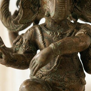 Op de afbeelding: Bronzen beeld van Ganesha, de hindoe&iuml;stische god. De sculptuur heeft meerdere armen en een olifantenkop met ingewikkelde details. Het beeld heeft een verweerde, antieke uitstraling.