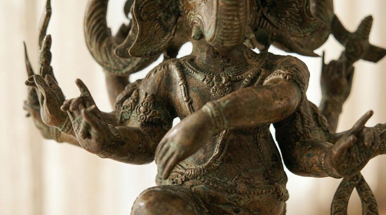 Op de afbeelding: Bronzen beeld van Ganesha, de hindoe&iuml;stische god. De sculptuur heeft meerdere armen en een olifantenkop met ingewikkelde details. Het beeld heeft een verweerde, antieke uitstraling.