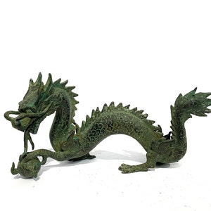 May include: A bronze-colored dragon figurine with a detailed, textured surface. The dragon has a long, serpentine body, a detailed head with a flowing mane, and a curled tail. The dragon is holding a sphere in its claws. The figurine is approximately 10 inches long.