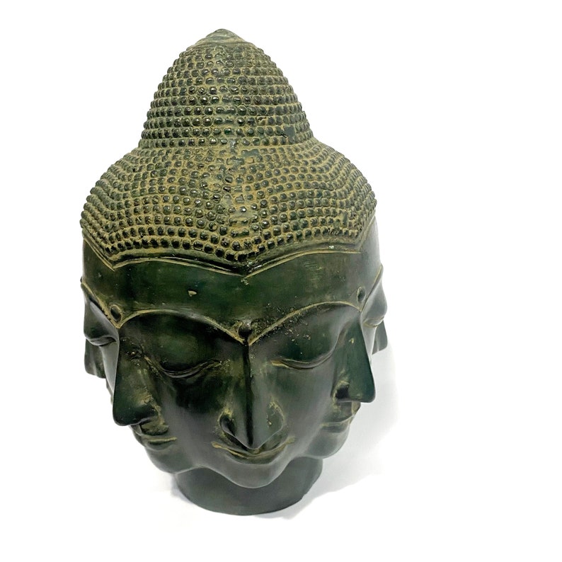 May include: A dark green Buddha head sculpture with four faces. The sculpture has a textured, detailed surface and a serene expression. The head is set against a white background.