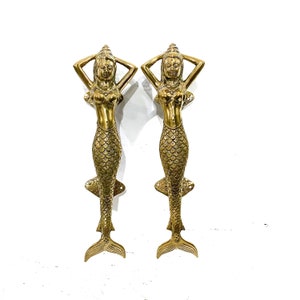May include: Two gold mermaid door handles with a detailed design. The mermaids are holding their hands above their heads and have a crown on their heads.