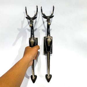 Può includere: Un paio di maniglie per porte in metallo nero a forma di cervo con dettagli dorati. Le maniglie sono lunghe e hanno un design decorativo.