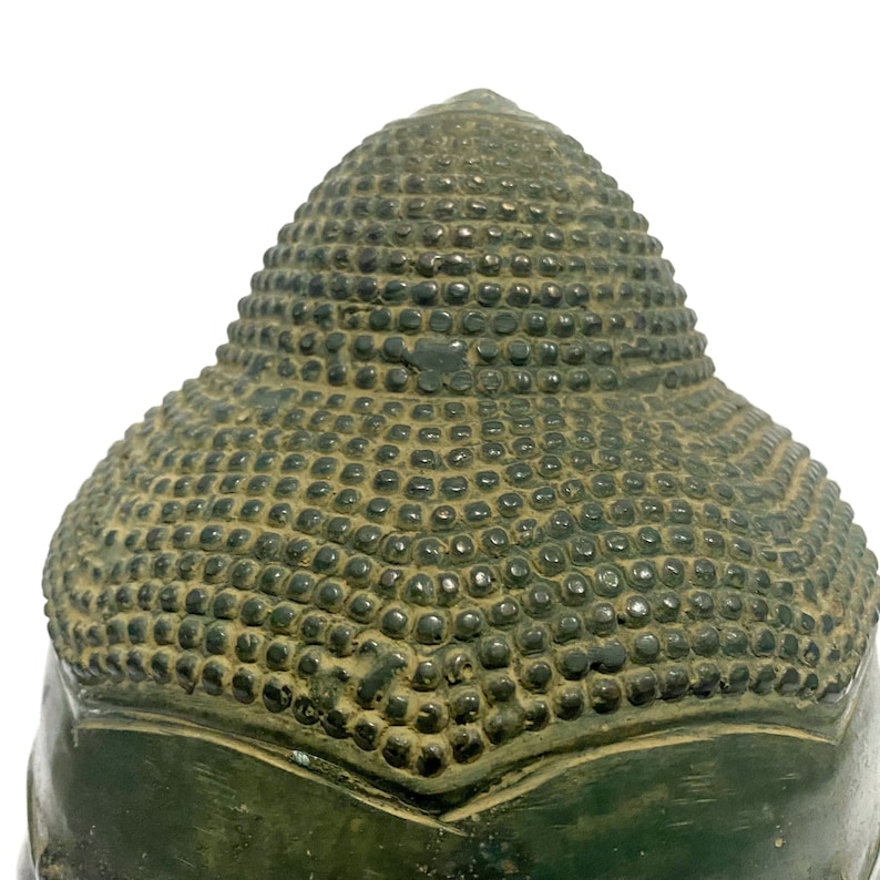 May include: Close-up of the back of a bronze Buddha head. The head features a detailed pattern of small, rounded bumps covering the top and back of the head. The bronze has a weathered, aged appearance with a dark green patina.