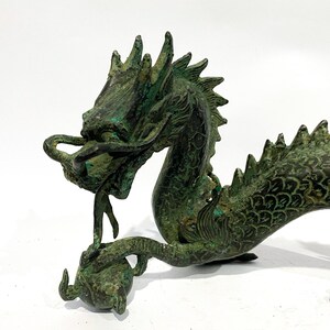May include: A detailed bronze dragon sculpture with a verdigris finish. The dragon is depicted with intricate scales, a flowing mane, and a curled tail. It is holding a sphere in its claw, showcasing a traditional Asian art style.