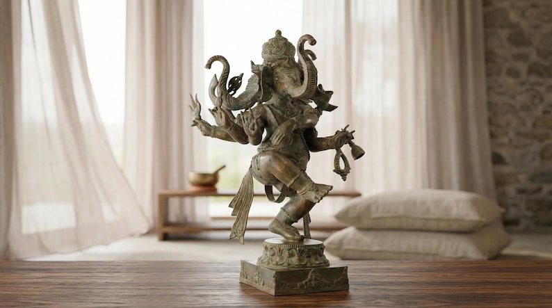 Op de afbeelding: Een bronskleurig standbeeld van de godheid Ganesha in een dansende houding met meerdere armen. De figuur heeft een olifantenkop, een kroon en ingewikkelde versieringen en staat op een vierkante voet met gedetailleerd houtsnijwerk.