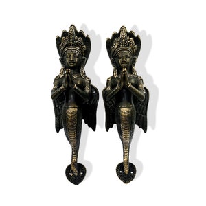 May include: A pair of ornate brass door handles in the shape of a woman with a snake tail. The woman is wearing a crown and has her hands clasped in prayer. The handles are a dark bronze color with gold accents.