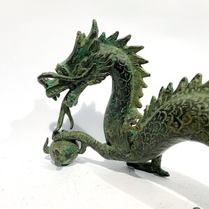 May include: A detailed bronze dragon sculpture with a verdigris finish. The dragon is holding a sphere in its claw and has a detailed, textured body. The sculpture is on a white background.