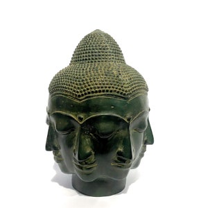 May include: A dark green Buddha head sculpture with four faces and a detailed, textured topknot. The sculpture has a weathered appearance, suggesting age or a vintage style. The faces are serene, with closed eyes and subtle features.